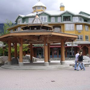 A timber gazebo on a plaza in Whistler Village, with lodge buildings and storefronts behind
