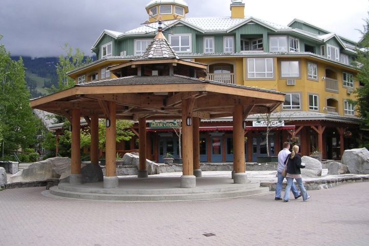 A timber gazebo on a plaza in Whistler Village, with lodge buildings and storefronts behind
