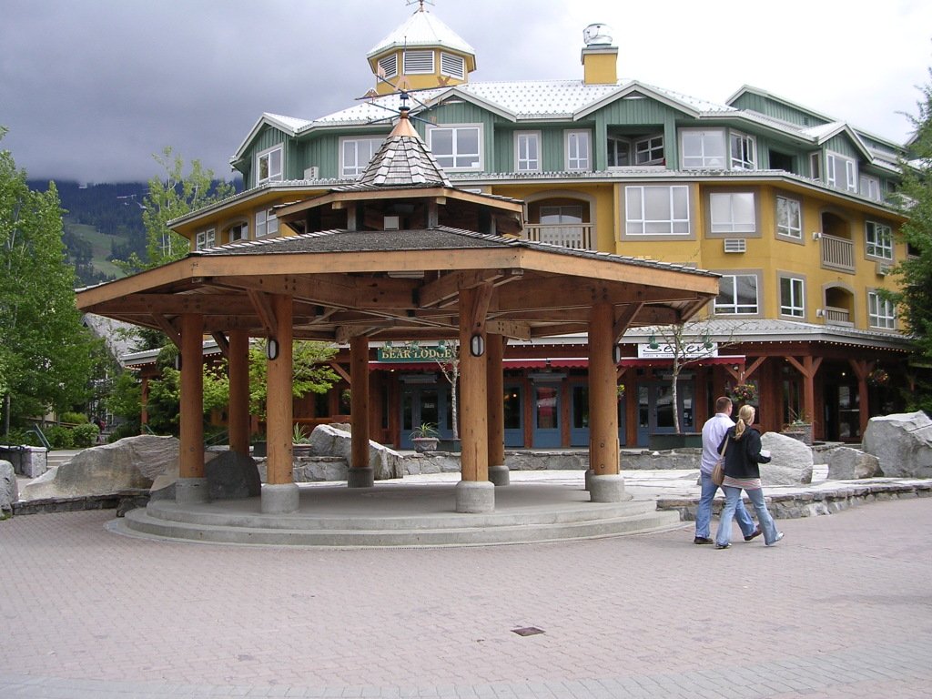 A timber gazebo on a plaza in Whistler Village, with lodge buildings and storefronts behind