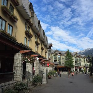 The pedestrian Village Stroll in Whistler Village, lined with stone-fronted shops and flower boxes, with snow on the peaks beyond