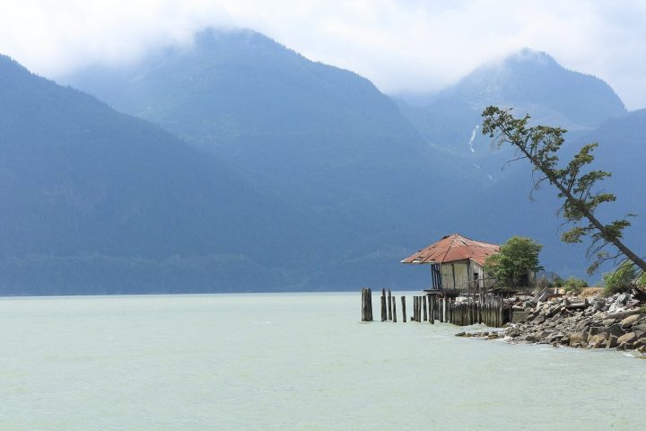 An old pier building on rocks at Britannia Beach, with Howe Sound and cloud-topped mountains behind