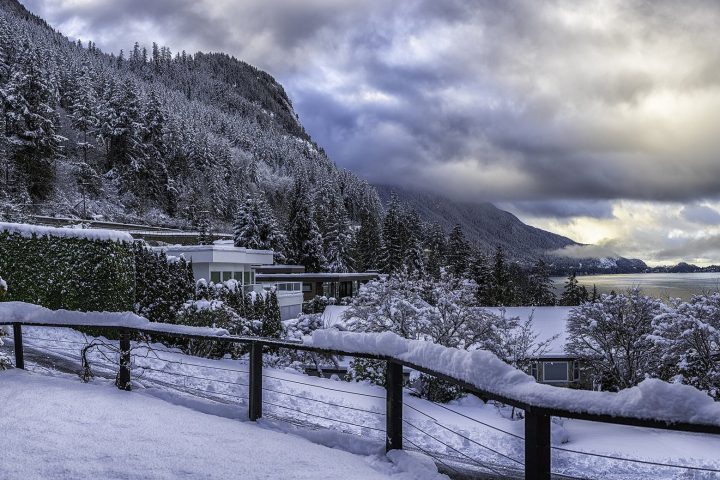 Fresh snow on trees, railings and rooftops on the shore of Howe Sound under heavy winter cloud
