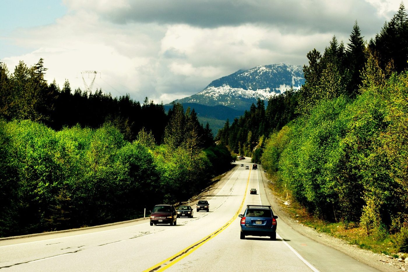 Cars on the Sea to Sky Highway between forested slopes, with a snow-dusted mountain ahead