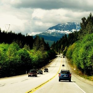 Cars on the Sea to Sky Highway between forested slopes, with a snow-dusted mountain ahead