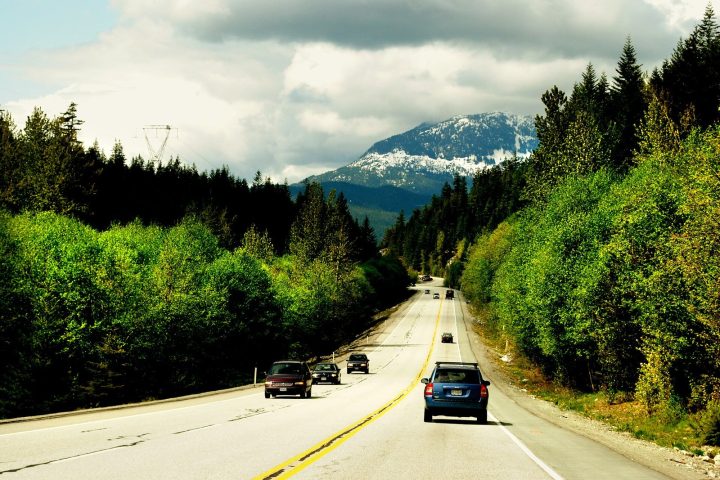 Cars on the Sea to Sky Highway between forested slopes, with a snow-dusted mountain ahead